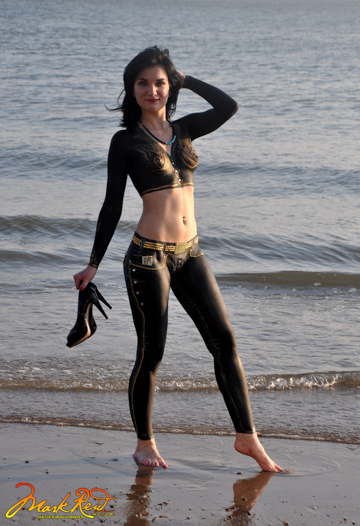 black haired woman body painted in a black sleeved vest with black jeans and gold highlights.